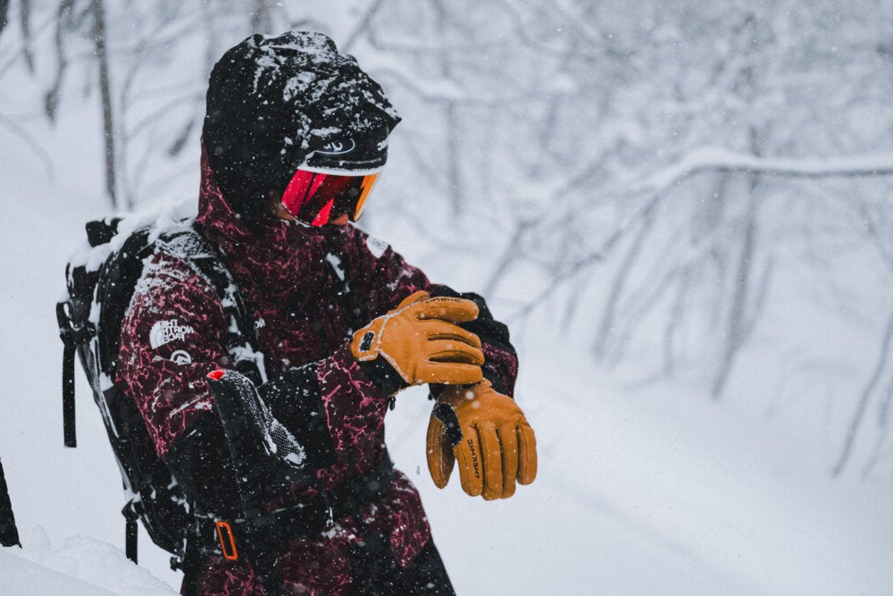 Person in winter gear with a backpack and heated gloves in a snowy landscape