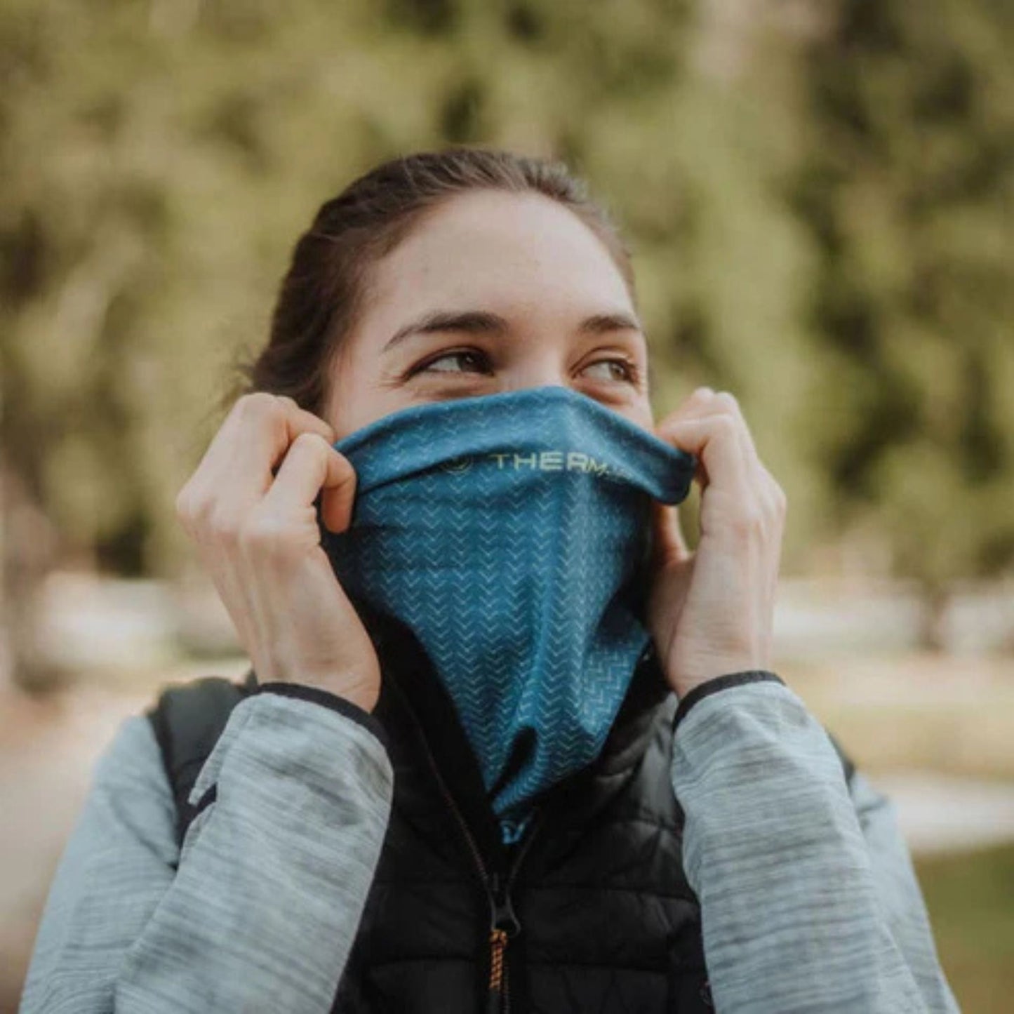 Person wearing a blue neck gaiter with a blurred natural background